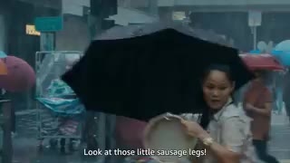 A woman in a black-and-white checked suit shops for luxury handbags in a store. The camera pans away from the shop window to a rainy street in Hong Kong, filled with people carrying umbrellas. A woman wearing a tan floral T-shirt talks to her unseen son on a video call.