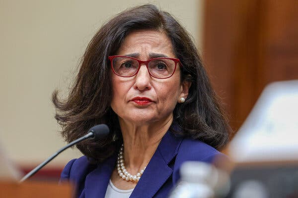 Nemat Shafik sits in front of a microphone, wearing a purple jacket and pearls. 