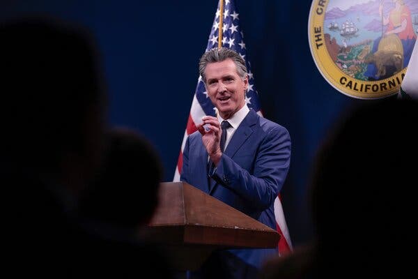 Gov. Gavin Newsom of California stands at a brown podium in front of an American flag and the state seal.