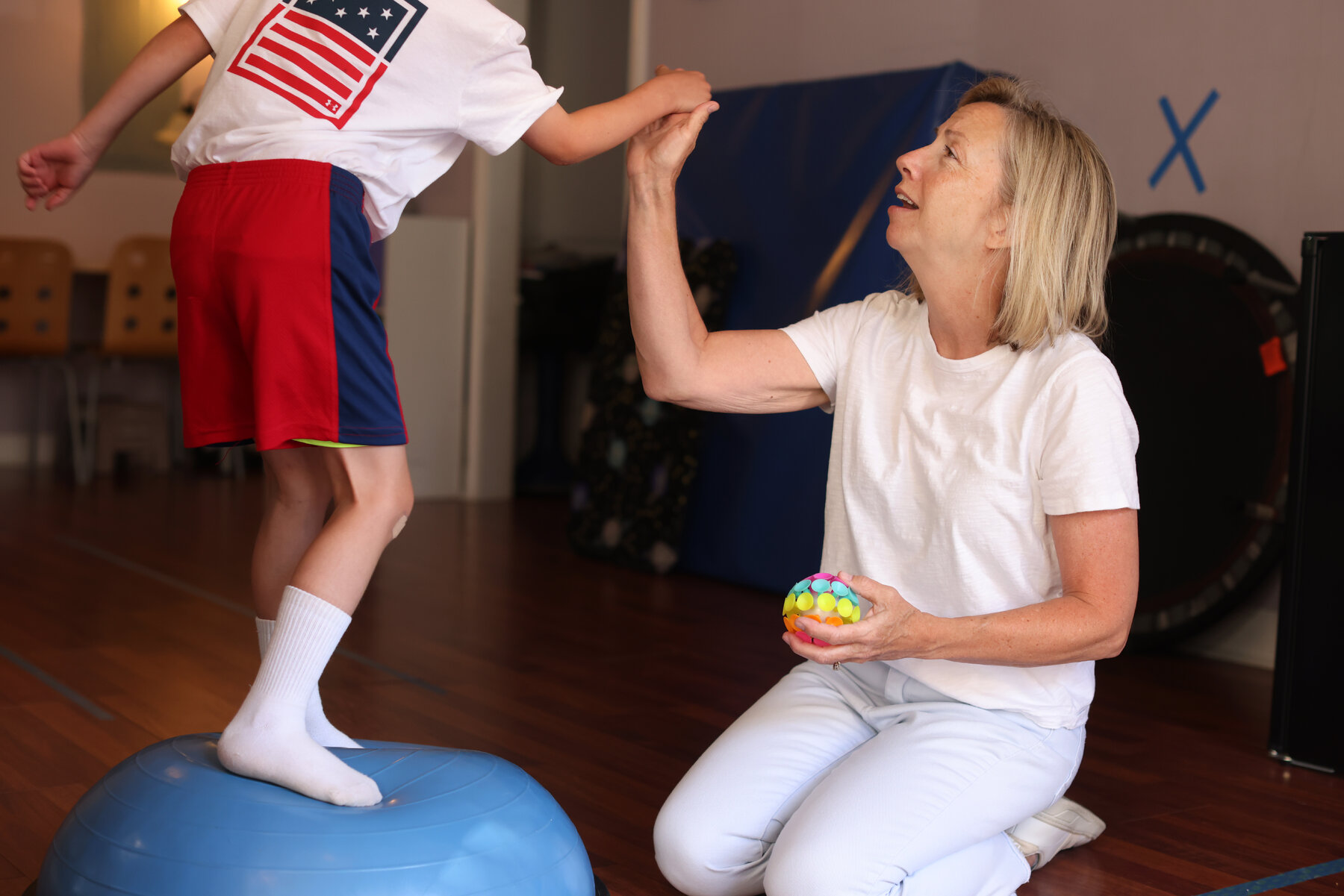 Heidi Tringali, an occupational therapist in Charlotte, N.C., holds hands with a child who is standing on a ball. 