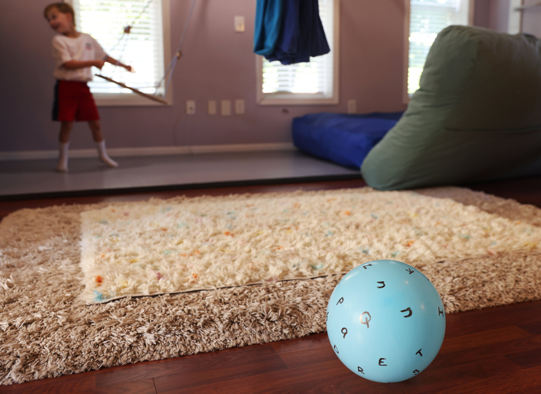 A child in a playroom holds a swing, with a bouncy ball in the foreground. 