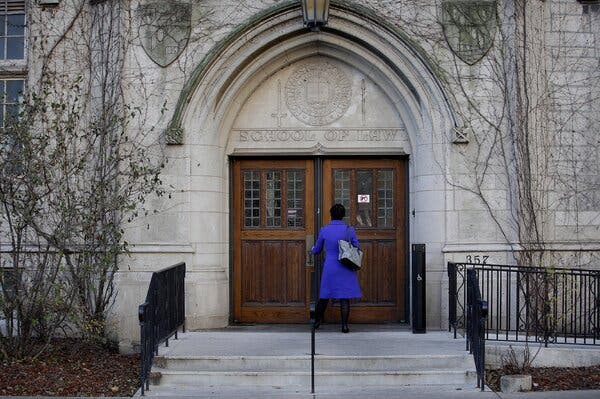 A person in a bright purple coat at wooden doors under a stone arch.