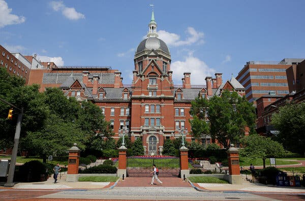 A man walks in front of a building at the Johns Hopkins Hospital Complex, which is a large, red-brick building. 