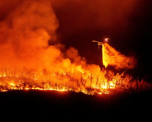 A helicopter dropping water on a burning forest.