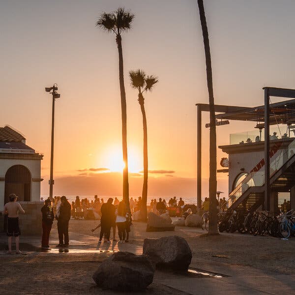 A crowd of people gather near a beach as the sun glows just above the horizon.