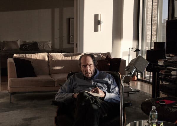 Philip Roth sits low in a large armchair and writes with a pen on a piece of paper resting in his lap. He is in his Manhattan apartment.