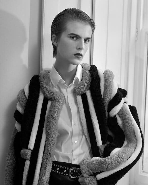 A model with slicked-back hair poses in a white collared shirt and a multi-colored fur jacket.