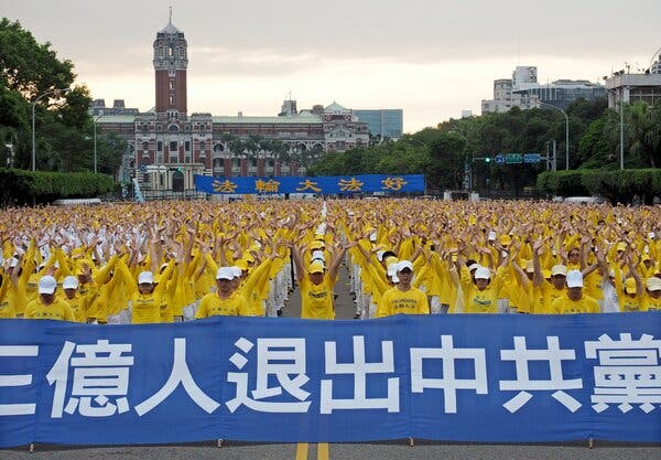 A crowd of Falun Gong practitioners in yellow shirts carry blue banners.