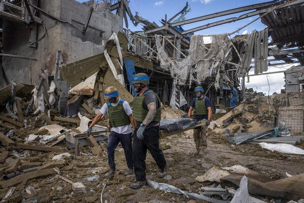 People in helmets and vests carrying a stretcher in the rubble of a ruined building.