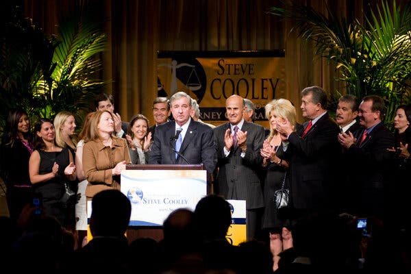 A man behind a podium with several people around him clapping.