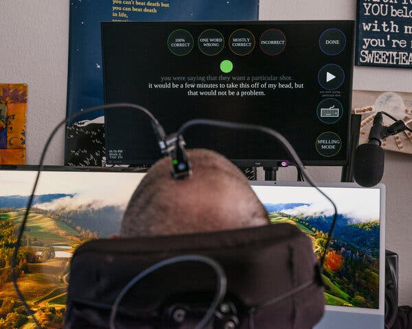 Mr. Harrell, seen from the back, faces several computer monitors. One shows a green dot and some text on the screen reading “It would be a few minutes to take this off of my head, but that would not be a problem.”