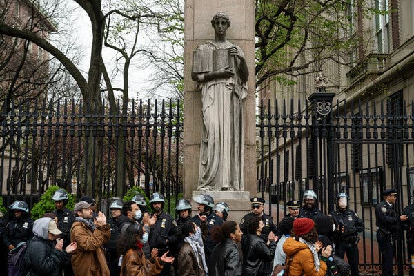 Protesters and police officers stand outside the gates of Columbia University.