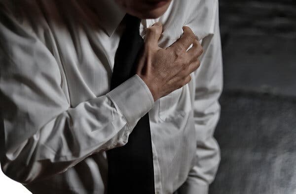 Man wearing a white shirt and tie holds his chest with his hand.