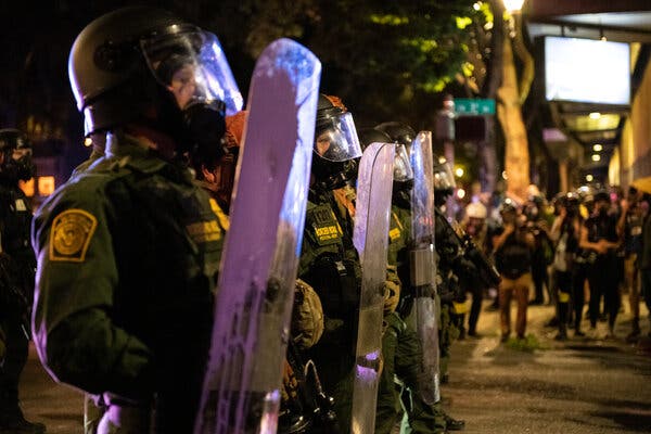 A row of people in military uniforms holding plastic shields on the street at night.