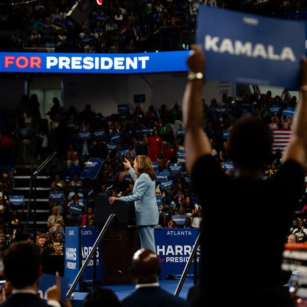 Kamala Harris speaks at a rally. A person holds up a “Kamala” sign in the foreground.