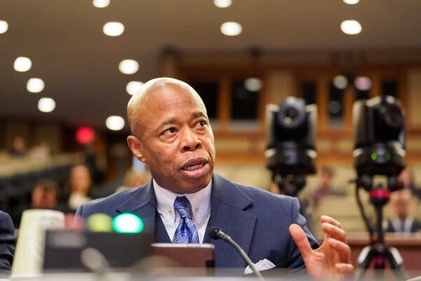 Mayor Eric Adams, wearing a purple suit and tie, speaks at a lectern.