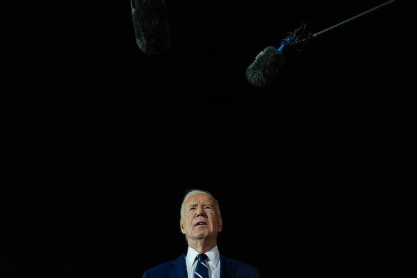 President Biden speaks in a suit, with microphones near him.