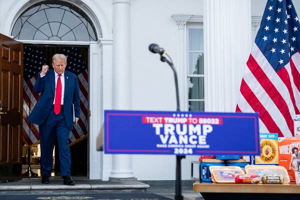 Donald Trump raises his right fist as he approaches a microphone set up next to a table filled with cereal and other grocery-store items.