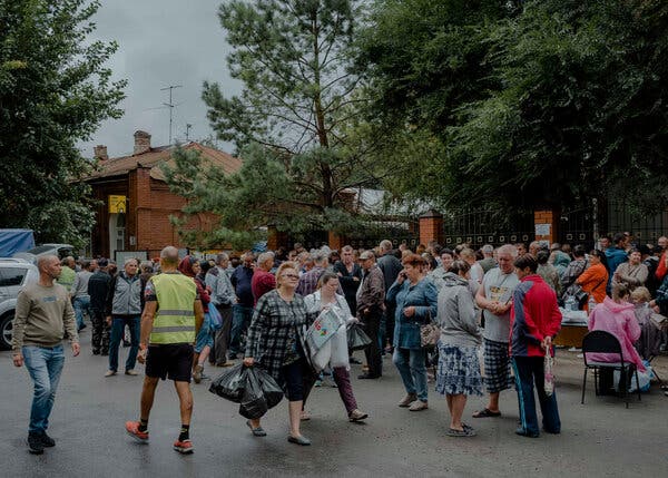 A crowd of Russians mostly stand or walk near a brick building during daytime hours.