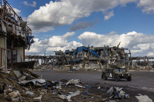 A Ukrainian military vehicle drives past destroyed buildings.