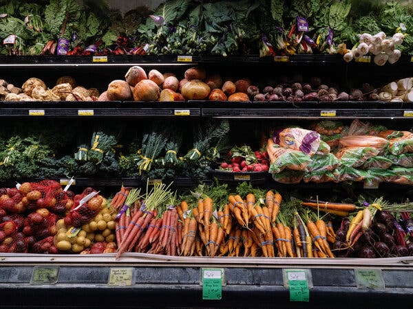 Produce shelves at a grocery store, with carrot bunches, bags of potatoes, leafy greens and other items.