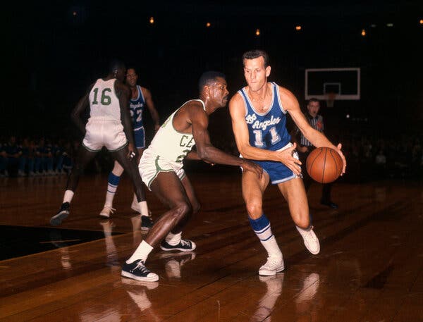 Frank Selvy, wears a blue No. 11 Lakers uniform as he dribbles the ball by a Celtics player who is wearing a white uniform with green trim.