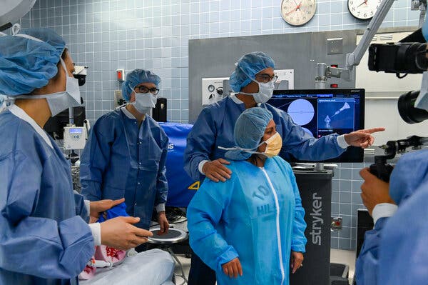 Doctors and nurses in scrubs, medical masks and hairnets stand in a hospital room.