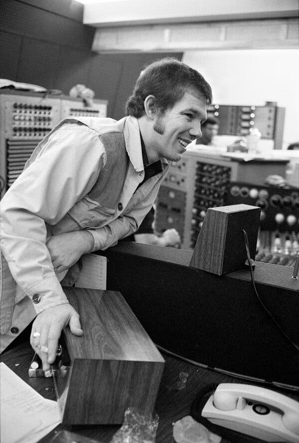 A black-and-white photo of Jerry Fuller, a young man with long sideburns and a vest, leaning on a piece of equipment in a recording studio control room.