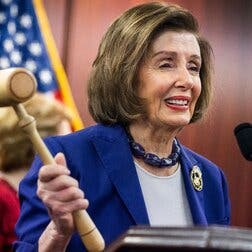 Representative Nancy Pelosi holds up a gavel (the one she used when the Affordable Care Act was passed), with an American flag in the background. 