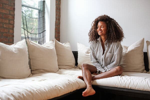 Kai Avent-deLeon smiles and looks toward a window as she sits on a couch in her home.