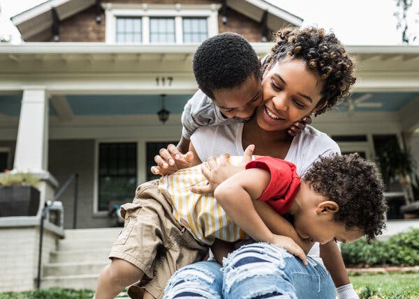 A woman and two children together in front of a two-story house.