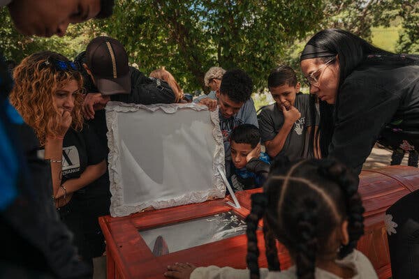 People standing over a coffin with a viewing window. 