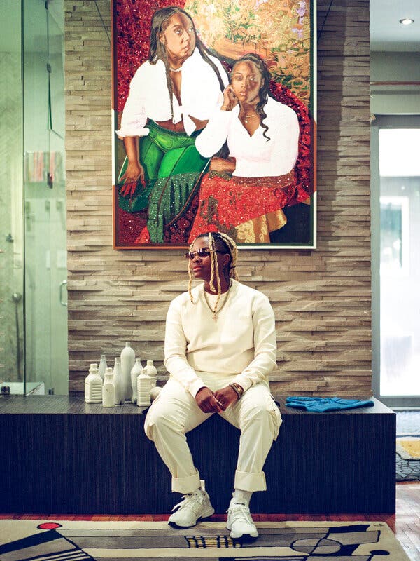 The artist Amani Lewis poses on a bench in front of their painting of two Black women in white shirts and vibrant skirts.