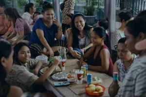 A group of Filipino women sit around a low table, eating and laughing.