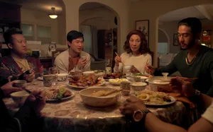 Michelle Yeoh sits at a round dining table with several young men including her sons, eating a meal.