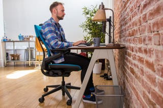 One of the authors sitting in the Steelcase Gesture sitting at a desk typing on a keyboard.