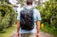 A person standing outside in a light blue short sleeve shirt wears the Cotopaxi Allpa 35L backpack, in black with a gray llama-head logo and aqua accents.