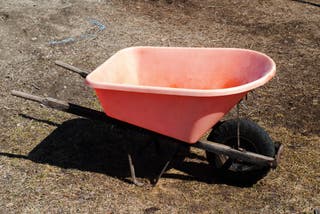 A clean red plastic wheelbarrow sitting in a dirt yard.