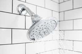 A clean and shiny stainless steel showerhead, that is installed in a bathroom and turned on.