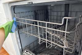 Close-up of a person using a sponge to clean the top rack of a dishwasher.