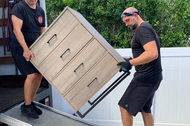 Two people lifting a dresser into a moving van.