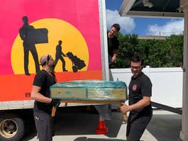 People carrying a coffee table near a moving truck.