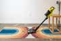 A vacuum cleaner leaning against a small wooden end table, in front of a pile of crumbs on a rainbow rug.