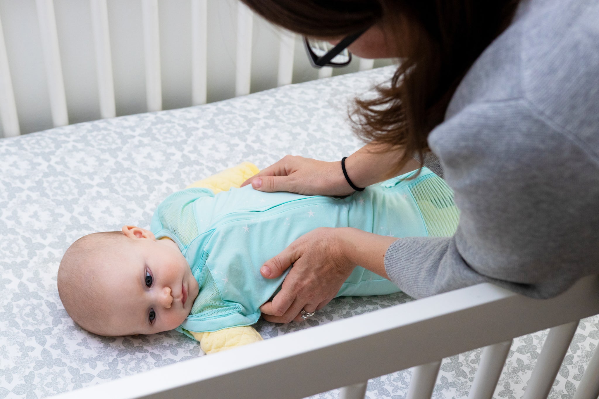 Close up of a person reaching to hold a baby in a crib.