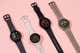 Four smartwatches laid out on a pink background.