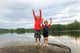 Two children wearing swim gear, standing side by side in front of a body of water.