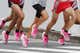 A bunch of runners wearing pink super shoes while jogging in the street.