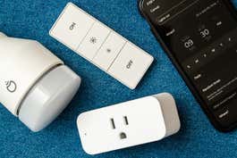 Three smart-home devices arrayed on a blue cloth next to a smart phone.